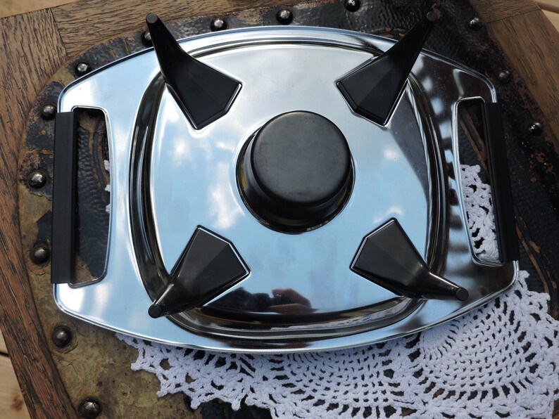 May include: A silver serving tray with four black triangular handles. The tray has a round, black center piece.