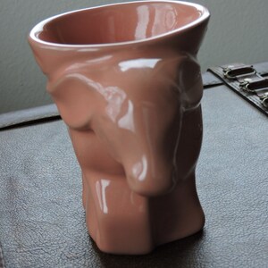 May include: A pink ceramic planter shaped like a dog's head. The planter has a smooth, glossy finish and is ideal for small plants or succulents.