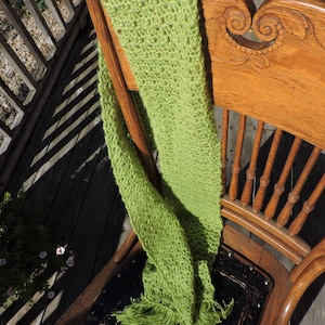 May include: A lime green crocheted scarf with fringe hanging over the back of a wooden chair.