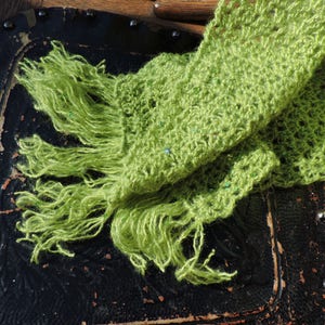 May include: A green crocheted scarf with a fringe. The scarf is draped over a wooden chair with a black leather seat.