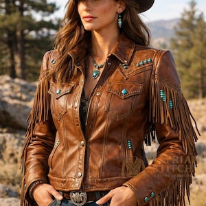 May include: A brown leather jacket featuring long fringe detailing on the sleeves, turquoise stone accents on the chest and shoulders, a collared neckline, and metal button closures. The jacket includes a logo with the text STRIAN STITCH.