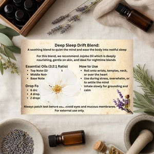 May include: An essential oil blend for restful sleep, with a white flower and lavender sprigs. The label reads "Deep Sleep Drift Blend" with instructions for use. Includes small brown bottles and a wooden box.