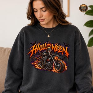 Peut inclure: Un sweat-shirt gris anthracite à col rond avec une impression graphique représentant un squelette sur une moto avec un phare en forme de citrouille. Le texte "HALLOWEEN" est écrit en orange au-dessus, entouré de flammes et de chauves-souris.