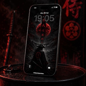 Peut inclure: Un smartphone affiche un fond d'écran sombre et dramatique avec un samouraï devant une lune rouge et des caractères japonais. Le téléphone est posé sur une surface sombre et texturée, avec un katana en arrière-plan. L'heure est 19h05.