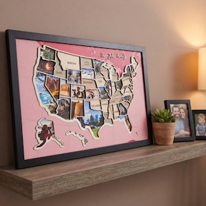 May include: A framed wall art piece featuring a wooden cutout map of the United States of America layered over a pink background. The map contains individual slots for photographs within each state, with the text The Yeh Family at the top centre.