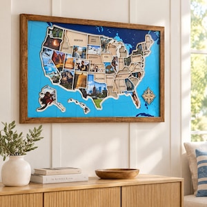 May include: A rectangular wall map of the United States featuring a wooden frame, a bright blue background with grid lines, and cutouts for each state. The map includes various personal photographs within the state borders and a compass rose.