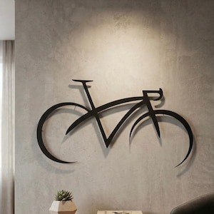 Op de afbeelding: Een zwart metalen wanddecoratie in de vorm van het silhouet van een racefiets. Het ontwerp bevat een minimalistisch frame, een stuur en gebogen wielbogen. De fietssculptuur is bevestigd aan een lichtgrijze muur boven een houten console.