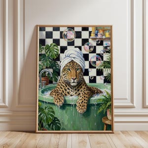 May include: A framed wall art print depicting a leopard with a white towel wrapped around its head, sitting in a green bathtub filled with water and bubbles. The background features a black and white checkered wall with green potted plants.