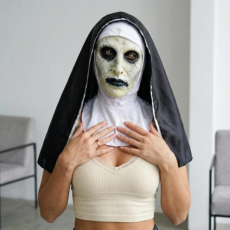 May include: A full-head nun mask featuring a pale, cracked, and weathered face with dark, sunken eyes and black lips. The mask includes an attached black and white habit headpiece that drapes over the shoulders, creating a realistic horror costume.