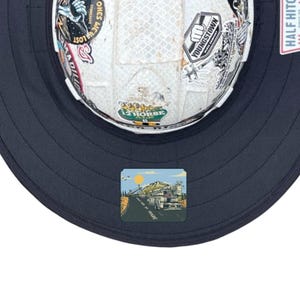 May include: A white hard hat with a dark navy brim, covered in various stickers including one that reads YOUNGSTOWN and another 12 HORSE ALE. A square graphic on the brim depicts a truck driving on a road toward mountains under a yellow sun.