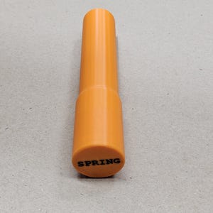 May include: An orange cylindrical object with the word "SPRING" printed in black on the bottom. The object has a wider base and a narrower top, and appears to be made of plastic.