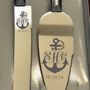 May include: A silver cake knife and server set with a decorative anchor and monogram. The anchor has a rope design and the monogram is "S H C". The date "12-18-14" is engraved on both pieces.