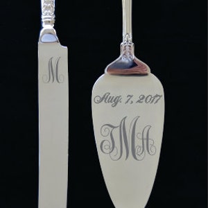 May include: Silver cake knife and server set with engraved initials and wedding date. The knife has the initial "M" engraved on the blade. The server has the initials "JMH" and the date "Aug. 7, 2017" engraved on the blade.