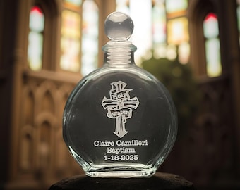 Może przedstawiać: Okrągła, przezroczysta butelka ze szkła z korkiem. Butelka jest grawerowana krzyżem i słowami "Holy Water". Butelka ma również wygrawerowany tekst "Claire Camilleri Baptism 1-18-2025".