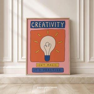 May include: A rectangular wall art print with a pink background featuring a central orange square containing a white lightbulb illustration with yellow rays. The text reads CREATIVITY at the top, and ISN'T MAGIC. IT'S PRACTICE. at the bottom.