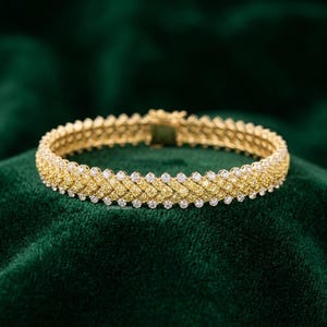 May include: A gold bracelet featuring a woven pattern of yellow stones bordered by rows of clear, round-cut stones. The piece includes a rectangular clasp mechanism and displays the text Sayani Gems in small print at the bottom center.