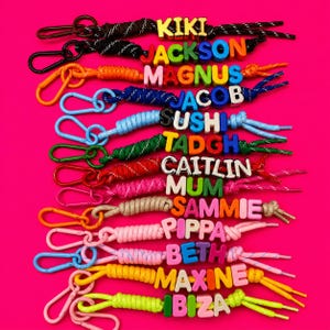 Puede incluir: Una colección de doce llaveros de paracord, cada uno con un mosquetón de metal o plástico y cuentas de letras de colores que deletrean nombres como KIKI, JACKSON, MAGNUS, JACOB, SUSHI, TADGH, CAITLIN, MUM, SAMMIE, PIPPA, BETH, MAXINE e IBIZA.