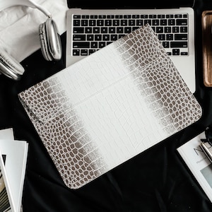 May include: A rectangular laptop sleeve featuring a white and grey crocodile skin texture pattern. The design transitions from a solid white center to a grey textured border. The sleeve has a flap closure and a structured, flat, envelope-style shape.
