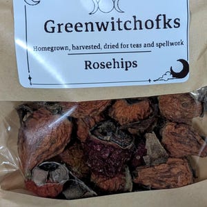 May include: A brown paper pouch containing dried rosehips with a white label that reads Greenwitchofks, Homegrown, harvested, dried for teas and spellwork, and Rosehips. The label features moon phase icons and a crescent moon graphic.