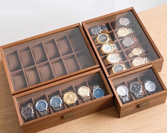 May include: Three wooden watch display cases with glass lids and brown interior compartments. One large empty case with twelve slots, one medium case with six watches, and one small case with three watches, all featuring metal latches.