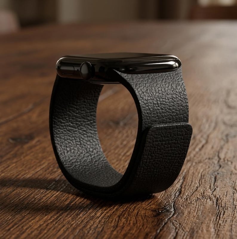 May include: A black smartwatch featuring a smooth, rectangular display case and a textured, matte black leather band. The watch is positioned in a circular shape, highlighting the grain of the strap and the side button on the dark casing.
