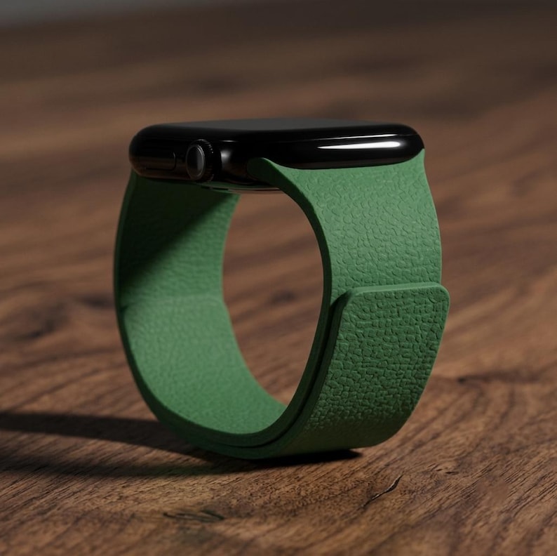 May include: A smartwatch with a black rectangular case and a textured green silicone band. The band features a smooth, matte finish with a distinct pebbled grain pattern, wrapping around to form a circular shape with a secure overlapping closure.