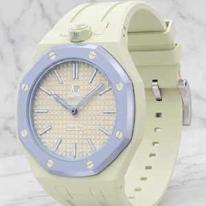 Puede incluir: Un reloj de pulsera amarillo pálido con un bisel octogonal morado claro y ocho tornillos plateados. La esfera tiene un patrón de cuadrícula, el texto AP, swatch y Royal Rip, con manecillas e índices plateados y una correa de silicona.