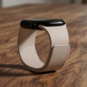 May include: A smartwatch with a glossy black rectangular case and a textured beige leather band. The band features a smooth, continuous loop design with a flat, overlapping closure section that secures the watch in a circular standing position.