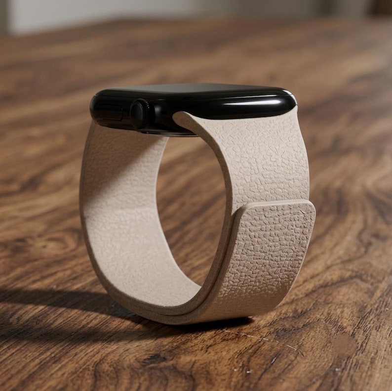May include: A smartwatch with a glossy black rectangular case and a textured beige leather band. The band features a smooth, continuous loop design with a flat, overlapping closure section that secures the watch in a circular standing position.
