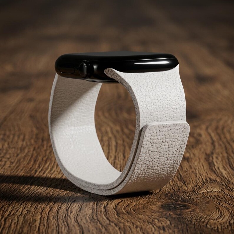 May include: A smartwatch featuring a glossy black rectangular case and a textured white strap. The strap has a pebbled surface finish and wraps around to form a circular loop. The side of the watch case displays a small circular digital crown button.