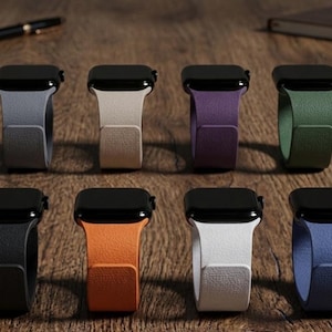 May include: Eight smartwatches arranged in two rows of four, each featuring a black rectangular screen and a textured silicone band in distinct colors including gray, beige, purple, green, black, orange, white, and blue.