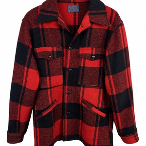 May include: A long-sleeved button-up jacket featuring a bold red and black buffalo plaid pattern. The garment includes a pointed collar, two chest pockets with buttoned flaps, two lower slash pockets, and a Pendleton brand label at the neck.