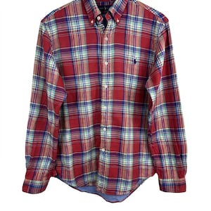 Può includere: Una camicia a quadri rossa, blu e gialla. La camicia a maniche lunghe ha un colletto button-down e un piccolo logo ricamato sul petto. La camicia è realizzata in un tessuto leggero.