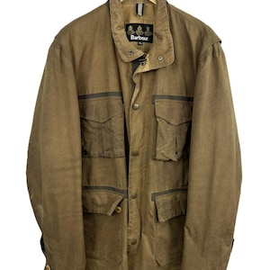 Op de afbeelding: Een beige jas van gewaxt katoen met een hoge kraag, een knoopsluiting aan de voorzijde en vier grote klepzakken op de borst en taille. Het binnenlabel toont de merknaam Barbour, met de maat XL duidelijk zichtbaar onder de tekst.