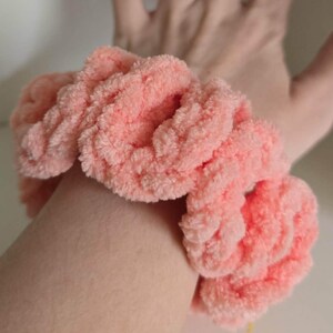 May include: A peach-colored scrunchie made from soft, plush, velvet-like yarn. The accessory features a thick, rounded, and textured construction with a gathered, ruffled appearance that creates a voluminous, circular shape around the wrist.