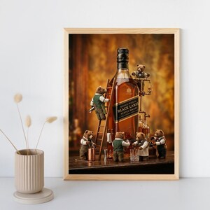 May include: A framed art print featuring a large bottle of Johnnie Walker Black Label Scotch Whisky surrounded by five small, anthropomorphic brown bears wearing vests and bow ties, with one bear climbing a wooden ladder against the bottle.