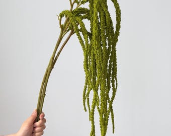 May include: A long, trailing artificial amaranth stem in a vibrant olive green color. The plant features multiple cascading, textured flower spikes that hang downward from a sturdy, smooth green stalk, creating a dense and flowing botanical display.