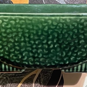 May include: A rectangular dark green ceramic planter with a textured, pebbled surface on the upper portion and vertical ribbed detailing along the base. The vessel features a distinct curved line separating the two textures, creating a structured form.