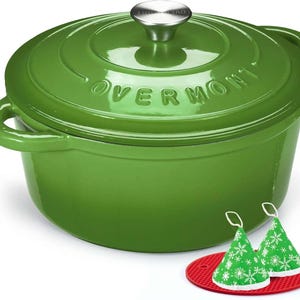 May include: A round, glossy green enamelled cast iron Dutch oven with a matching lid featuring the embossed text OVERMONT and a silver-coloured knob. Included are two green cone-shaped fabric pot holders with white snowflake patterns.