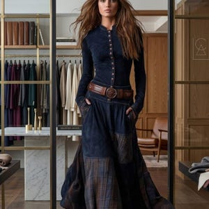 Può includere: Un top a maniche lunghe blu navy con bottoni abbinato a una gonna lunga blu navy coordinata con inserti patchwork a quadri marroni. L'outfit è stretto in vita da un'ampia cintura in pelle marrone con fibbia circolare e stivali stringati marroni.