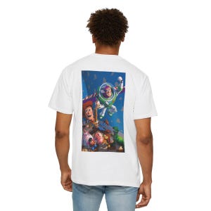 Może przedstawiać: Biała koszulka z kolorową grafiką postaci z filmu Toy Story, w tym Buzzem Astralem i Chudym. Projekt umieszczono na tle niebieskiego nieba. Ta codzienna koszulka jest odpowiednia do codziennego użytku.