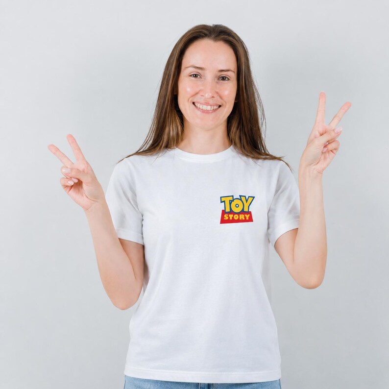 Może przedstawiać: Biała koszulka z logo "Toy Story" w kolorze ż&oacute;łtym, niebieskim i czerwonym. Koszulka ma kr&oacute;tkie rękawy i jest wykonana z miękkiego materiału. Logo znajduje się na lewej piersi.