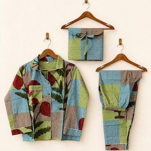 May include: A long-sleeved button-down shirt, matching trousers, and a folded fabric pouch, all featuring a checkered pattern in blue, green, and brown with large red floral motifs. Each item is displayed on a wooden hanger against a plain wall.