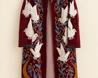 May include: A long, deep red velvet coat featuring intricate embroidery of white birds, blue leaves, and golden crescent moons. The open-front garment has a mandarin collar and is lined with a white and red vertical pinstriped fabric.