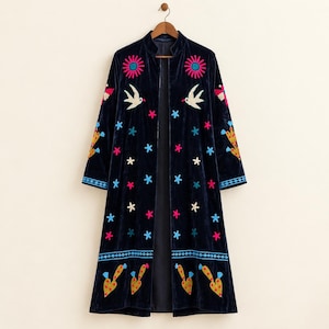 May include: A dark navy blue velvet duster coat featuring an open front and long sleeves. The garment is decorated with colorful embroidered motifs including pink flowers, white birds, small blue and white stars, and yellow cactus shapes.
