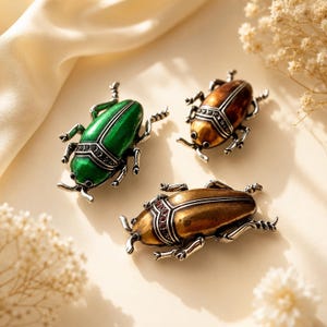 May include: Three beetle-shaped brooches featuring metallic finishes in green, bronze, and gold. Each insect pin displays intricate silver-toned legs, a segmented body, and a row of small dark stones embedded along the thorax area of the design.