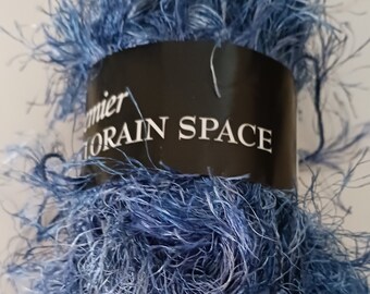 May include: A skein of blue fuzzy yarn with a black label that reads "Premier  Lorain Space".
