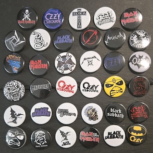 May include: A collection of thirty-five circular pin-back buttons featuring various heavy metal band logos and graphic illustrations, including Iron Maiden, Ozzy Osbourne, Black Sabbath, and Metallica, displayed in a grid arrangement.