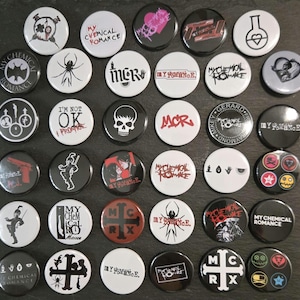 May include: A collection of thirty-five circular pin-back buttons featuring various My Chemical Romance band logos, spider motifs, skull illustrations, and song titles like I'm Not Okay, displayed in a grid arrangement with black and white designs.