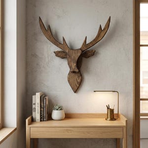 Può includere: Decorazione da parete a forma di testa di cervo in legno con grandi corna. La testa di cervo è montata su una parete grigio chiaro sopra una scrivania in legno. Una piccola pianta grassa e dei libri sono sulla scrivania.